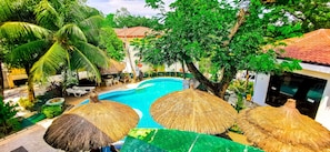 A swimming pool surrounded by thatched umbrellas, palm trees, and a garden area with outdoor furniture. - Cebu Hilltop Hotel (Cebu City)