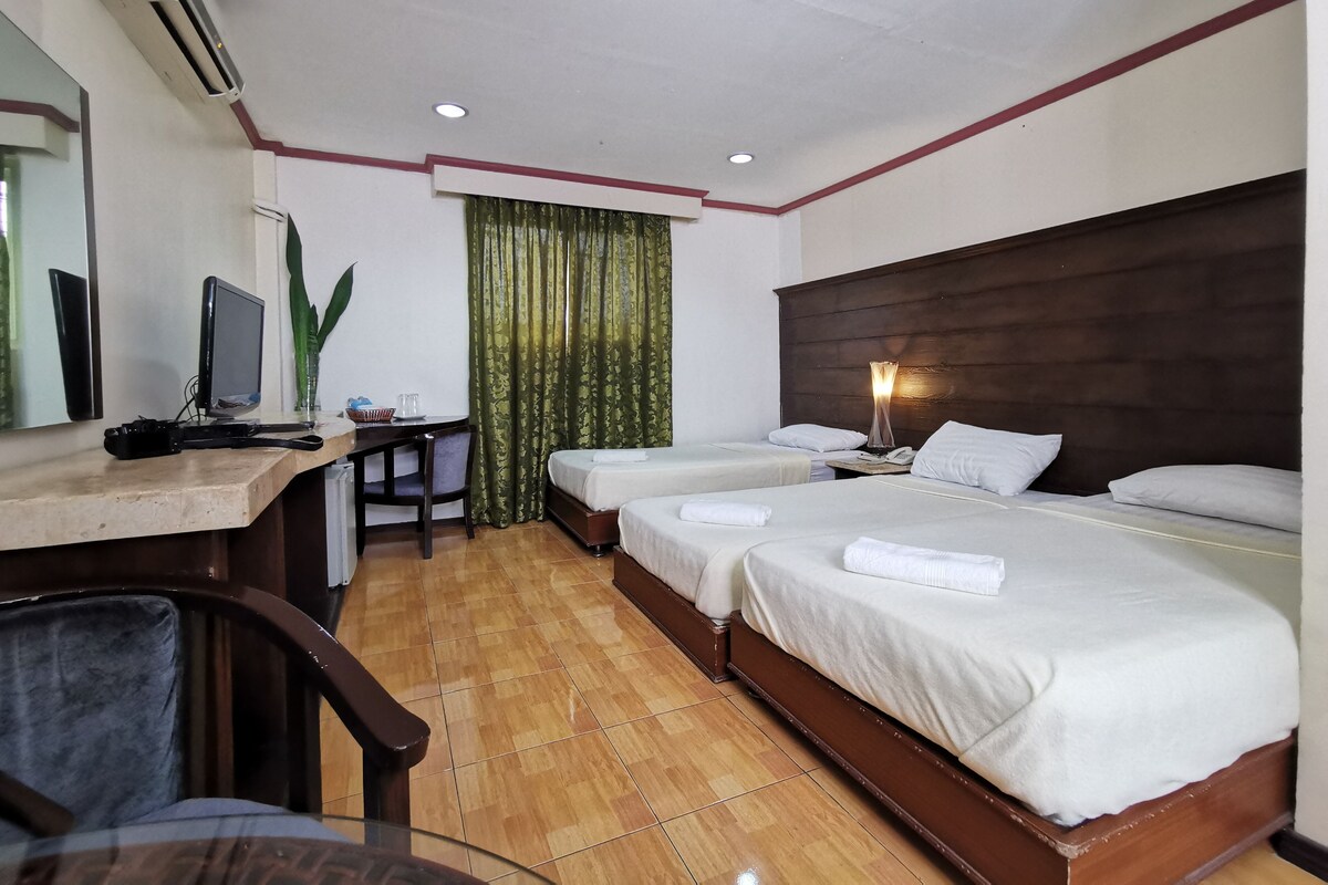 Quarto de hotel com duas camas, uma escrivaninha com computador, uma cadeira e uma televisão.