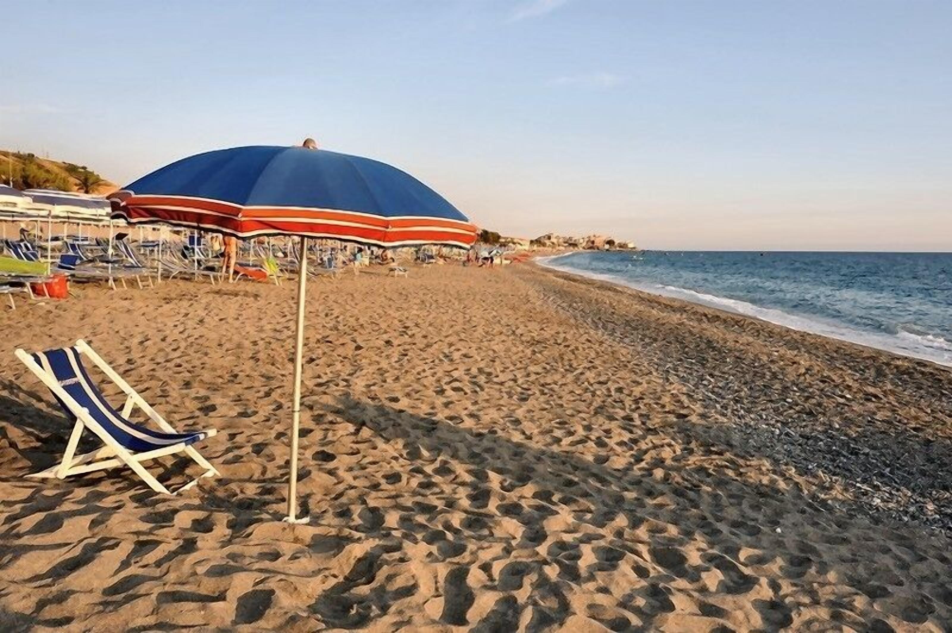 Una spiaggia con una fila di sedie a sdraio e ombrelloni, un cielo sereno e l'oceano sullo sfondo.