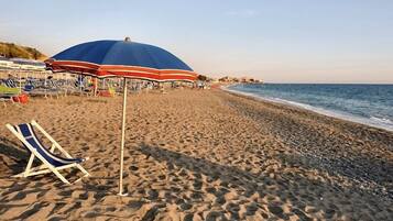 Una spiaggia con una fila di sedie a sdraio e ombrelloni, un cielo sereno e l'oceano sullo sfondo.