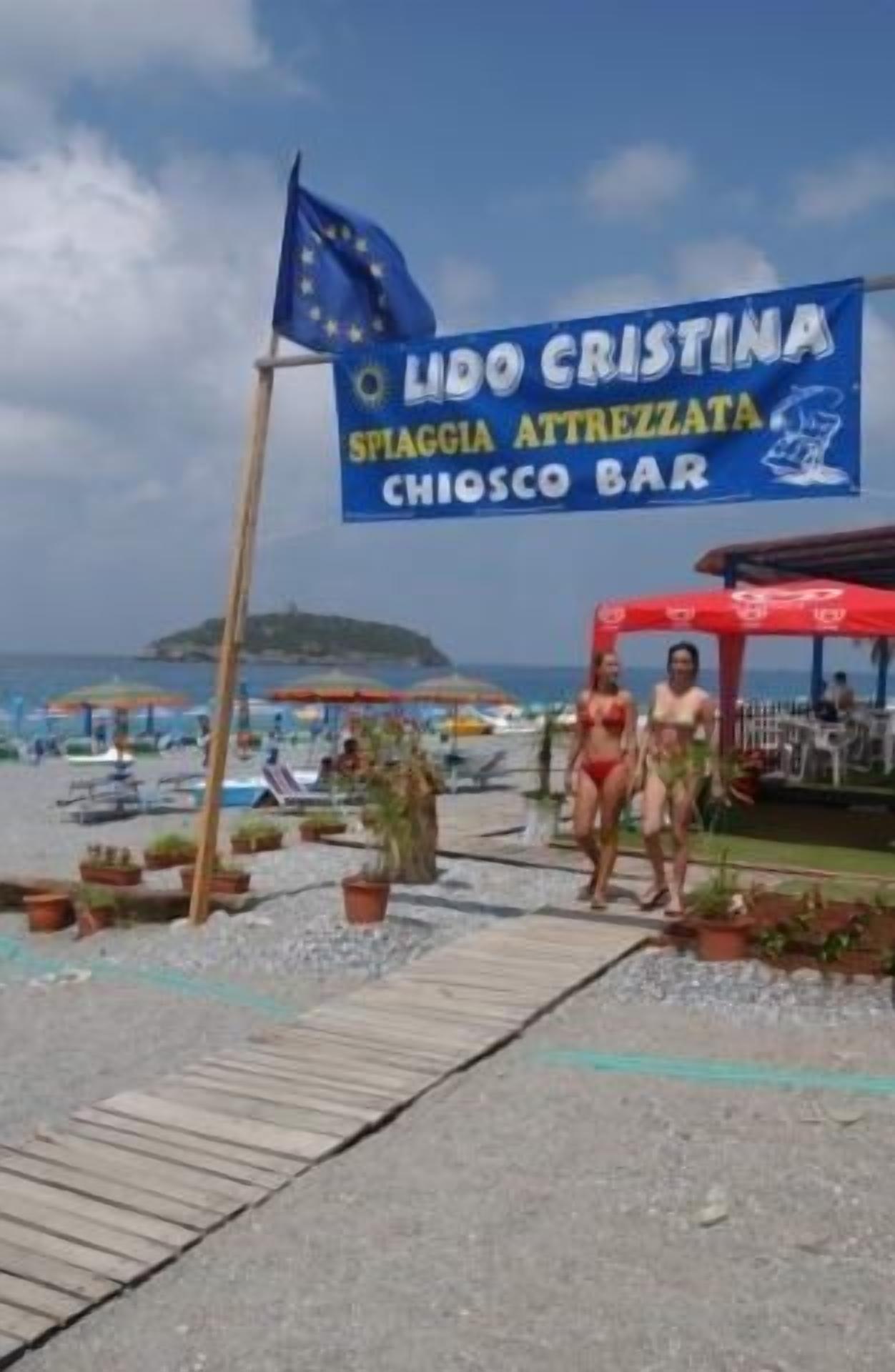 A beachside bar named Lido Cristina with a signboard, outdoor seating, and potted plants.