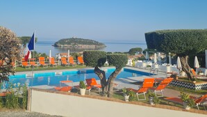 Zona de piscina con sillas de descanso anaranjadas, una bandera y vistas al mar y una isla distante.