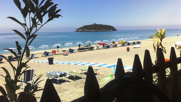 Una playa con sombrillas, sillas de descanso y una pequeña isla a lo lejos.