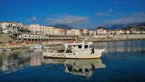 Un puerto con un barco blanco amarrado, edificios a lo largo del muelle y un cielo azul despejado.