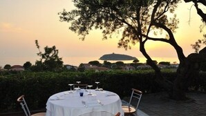 Un área de comedor al aire libre con una mesa redonda dispuesta para cuatro personas, rodeada de sillas, con vistas panorámicas a un cuerpo de agua y terreno distante.