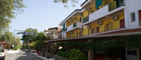 Un hôtel à la façade jaune, doté de balcons, d’une terrasse et d’une enseigne indiquant « Hôtel Cristina ».