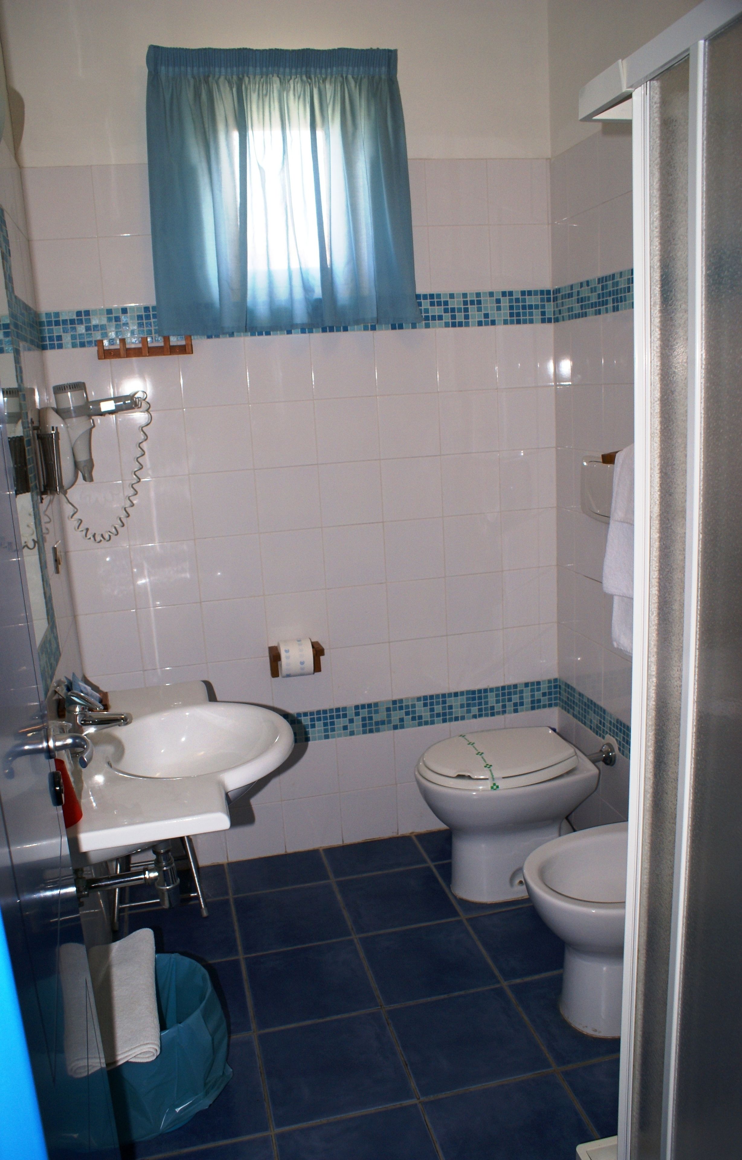 Un bagno con un lavandino, due servizi igienici, una doccia e un pavimento piastrellato di blu.
