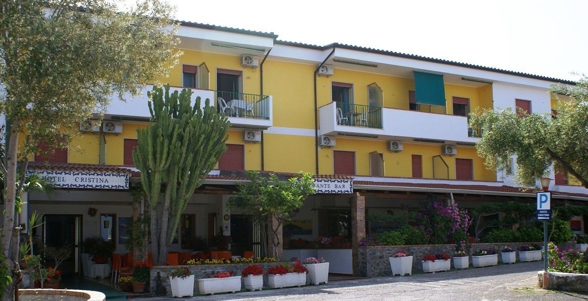 Un immeuble jaune doté de balcons et d’une enseigne indiquant « Hôtel Cristina ».