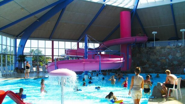 An indoor water park with a large pool, slides, and a covered area with seating.