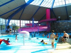 An indoor water park with a large pool, slides, and a covered area with seating.