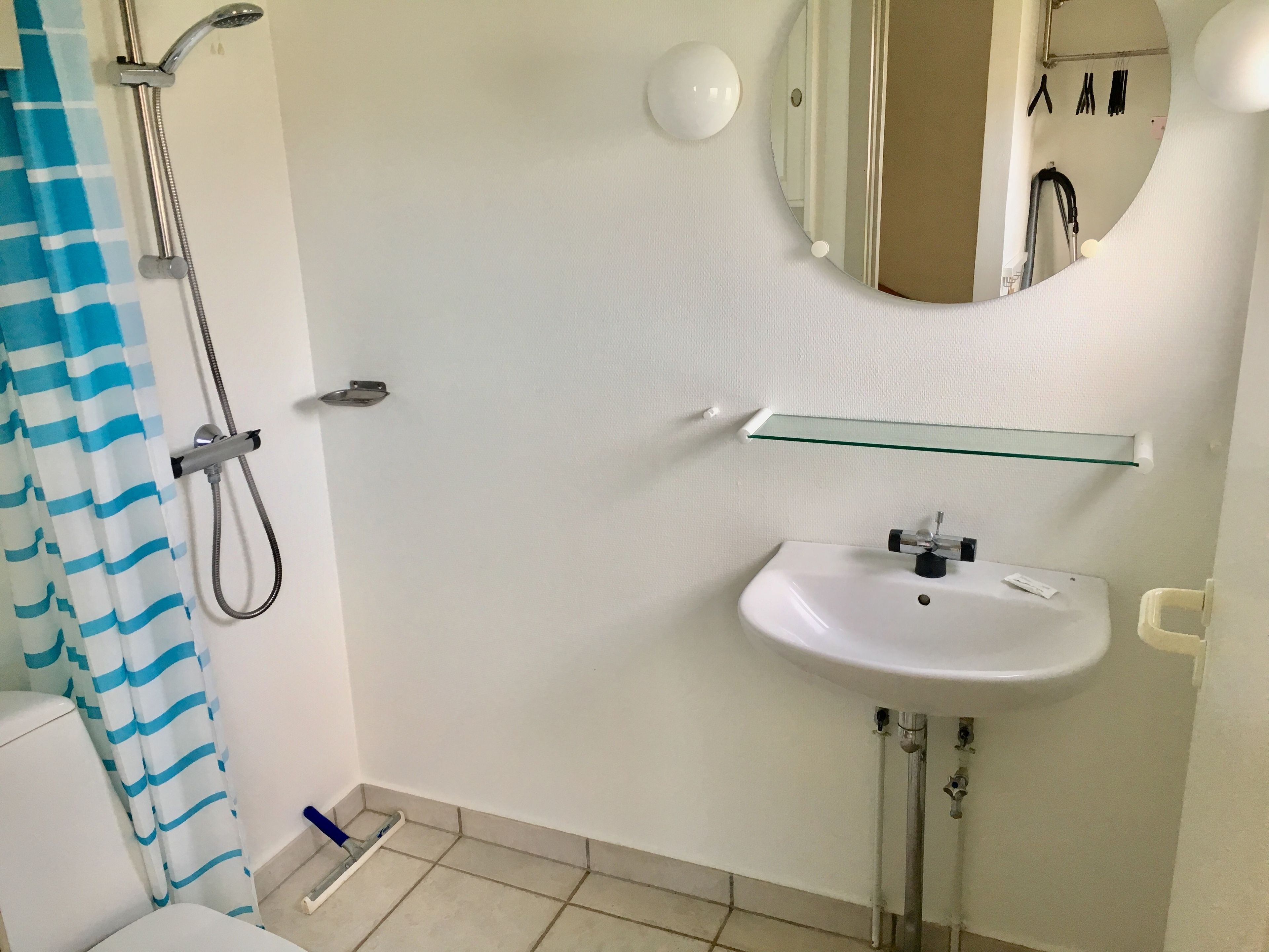 Une salle de bain avec une douche, un lavabo, un miroir et une étagère en verre.
