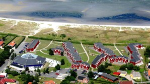 An aerial view of a coastal village with red houses, a large blue building with a dome, and a sandy beach.