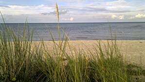 A beach with sand and grass in the foreground, and a calm sea in the background.