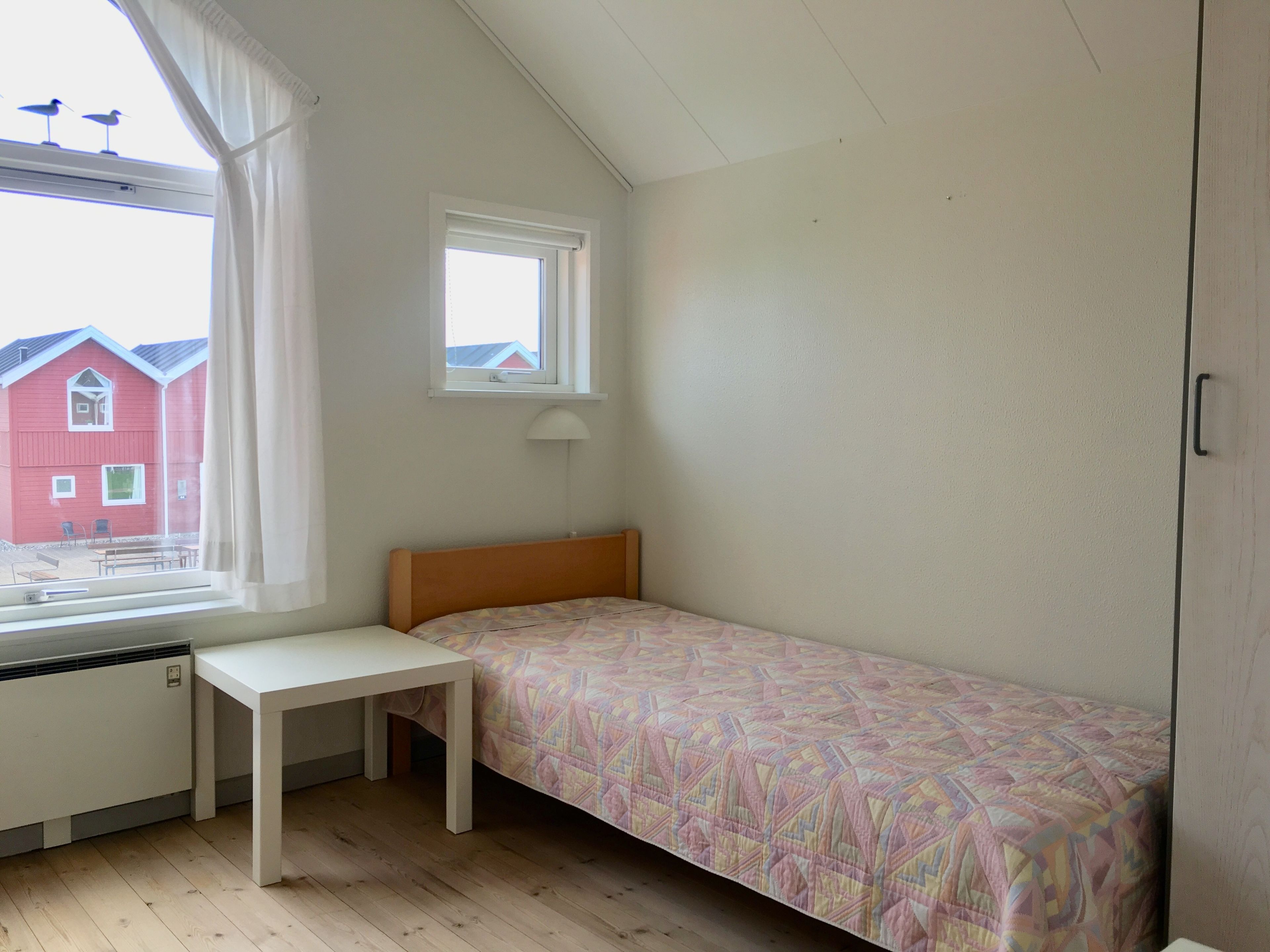 Un dormitorio pequeño con una cama individual, una ventana con cortinas, un escritorio y un radiador.
