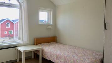 Un dormitorio pequeño con una cama individual, una ventana con cortinas, un escritorio y un radiador.