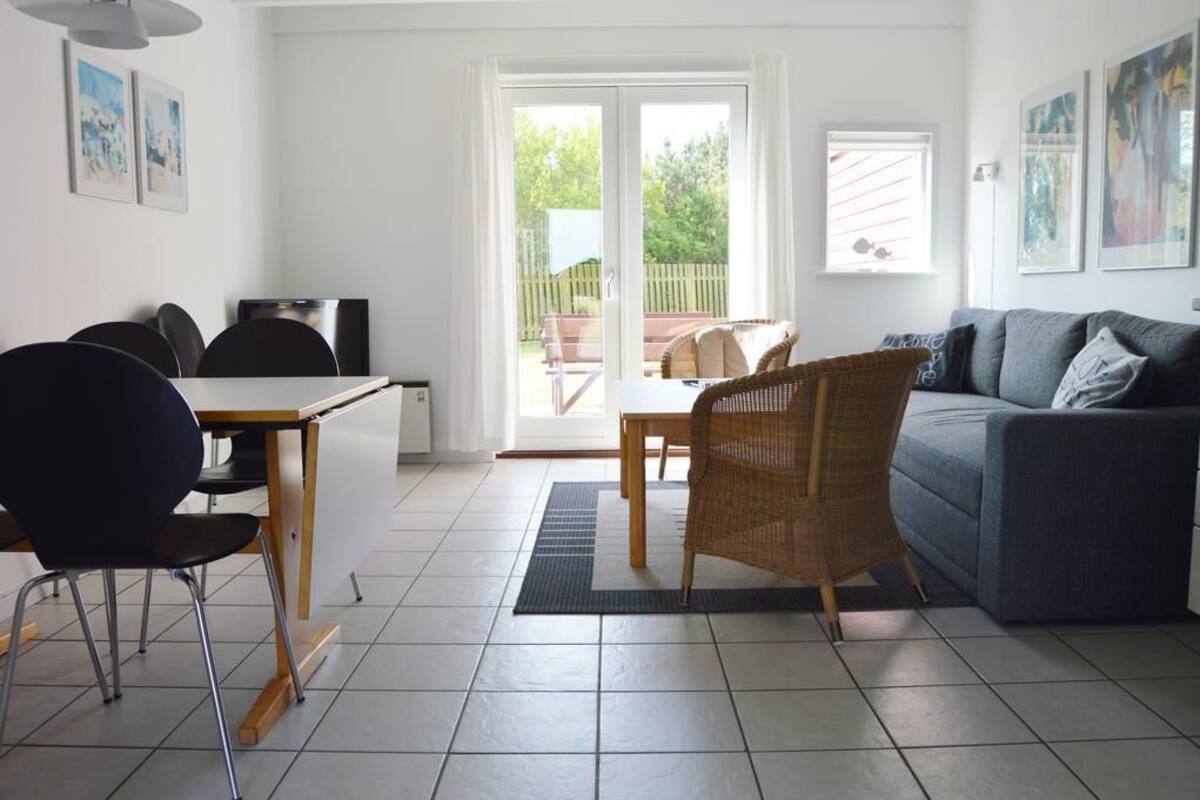 Ein Wohnzimmer mit einer Couch, einem Esstisch mit Stühlen, einem Fernseher und einer Glasschiebetür zu einem Außenbereich.