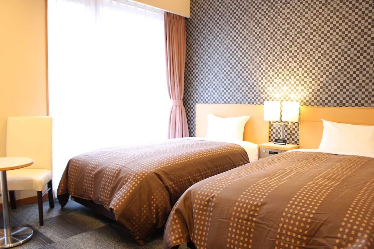 A hotel room with two beds, a small table, and a nightstand with lamps.