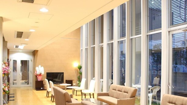 A spacious lounge area with multiple sofas and chairs, a flat-screen TV, and large windows offering a view of the outdoors. - Hotel Livemax Chiba Mihama (Chiba)