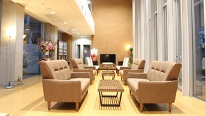 A spacious lobby with multiple seating areas, a flat-screen TV, and a large window providing a view of the outdoors. - Hotel Livemax Chiba Mihama (Chiba)