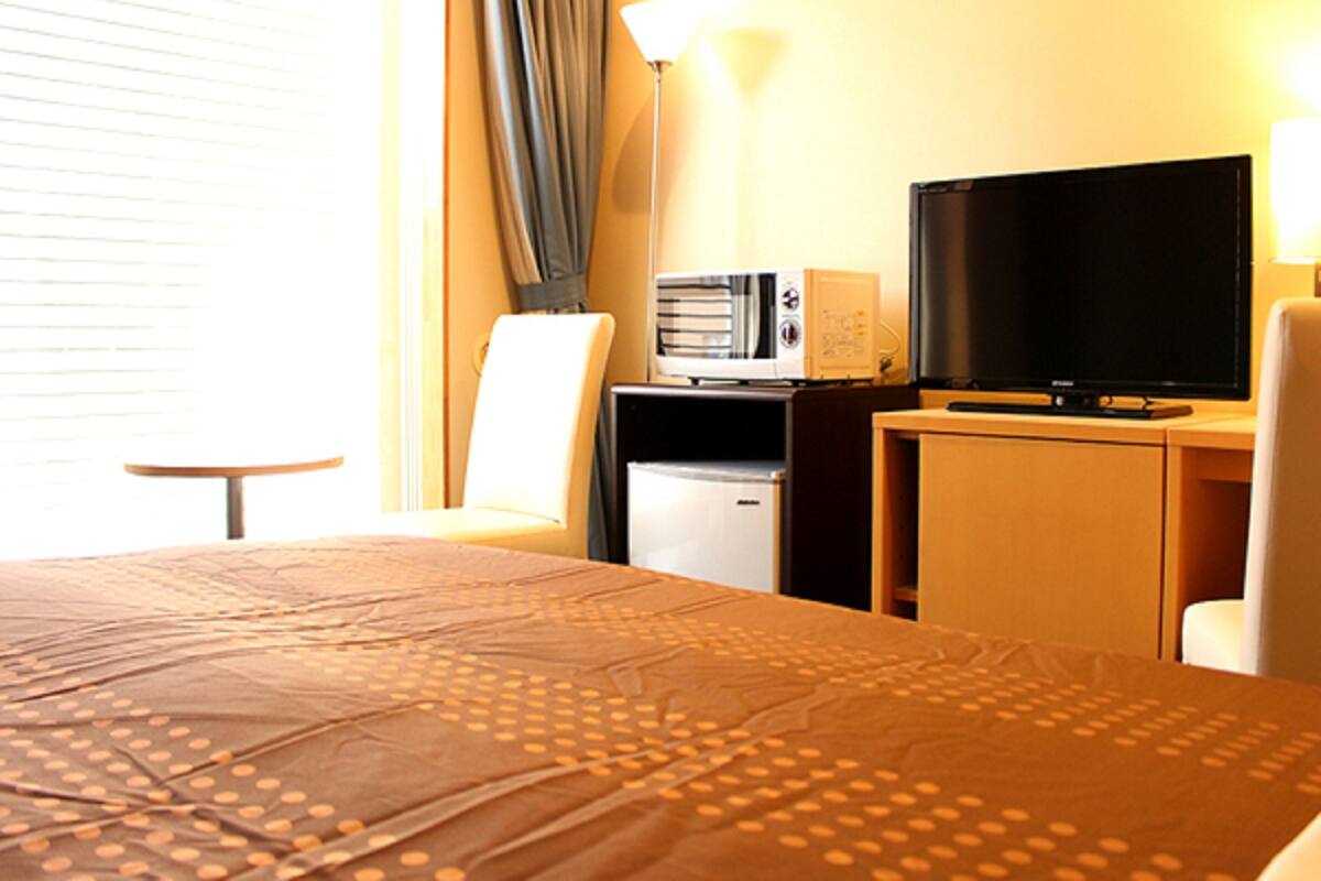 A hotel room with a bed, a desk with a television, a microwave, and a small refrigerator.