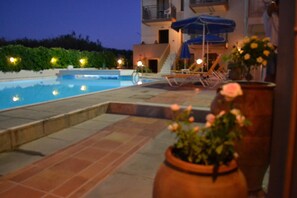 A swimming pool with lounge chairs and a slide, surrounded by potted plants and a building with balconies. - Alexandros M (Platanias)