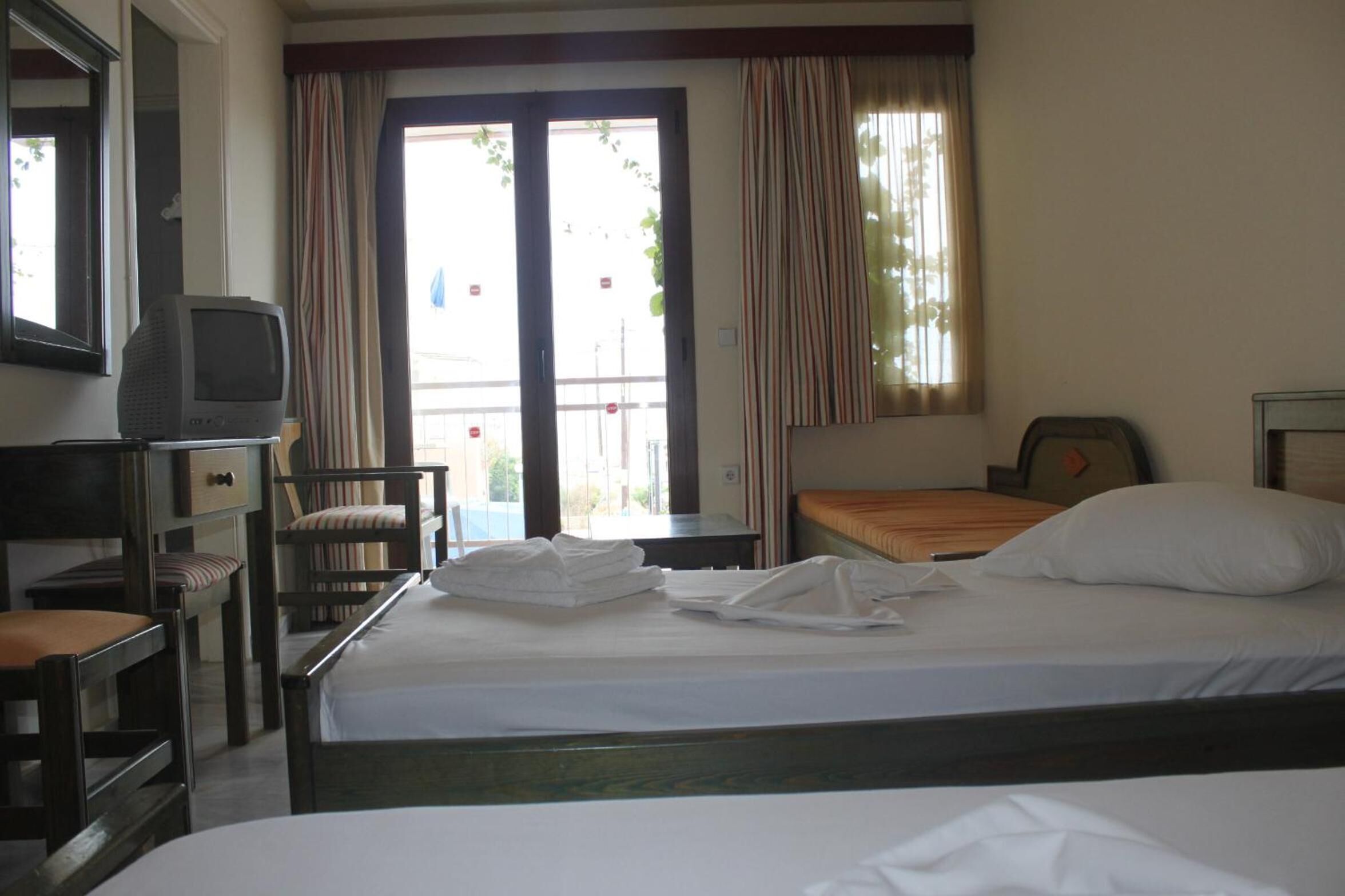 Ein Hotelzimmer mit Bett, Schreibtisch, Stuhl, Fernseher und einem Fenster mit Vorhängen.