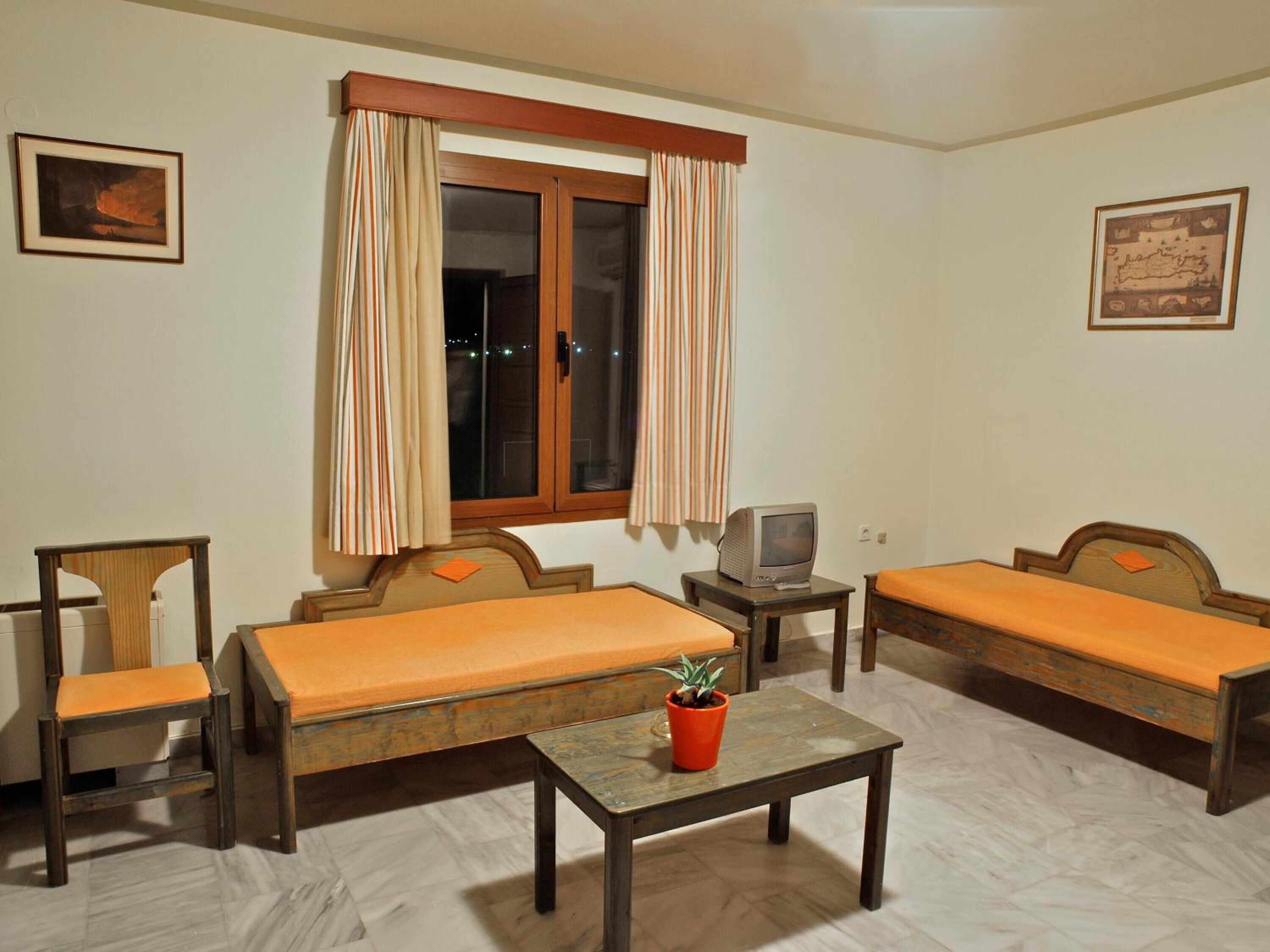 A room with two single beds, a small table with a potted plant, a television on a side table, and a window with curtains.