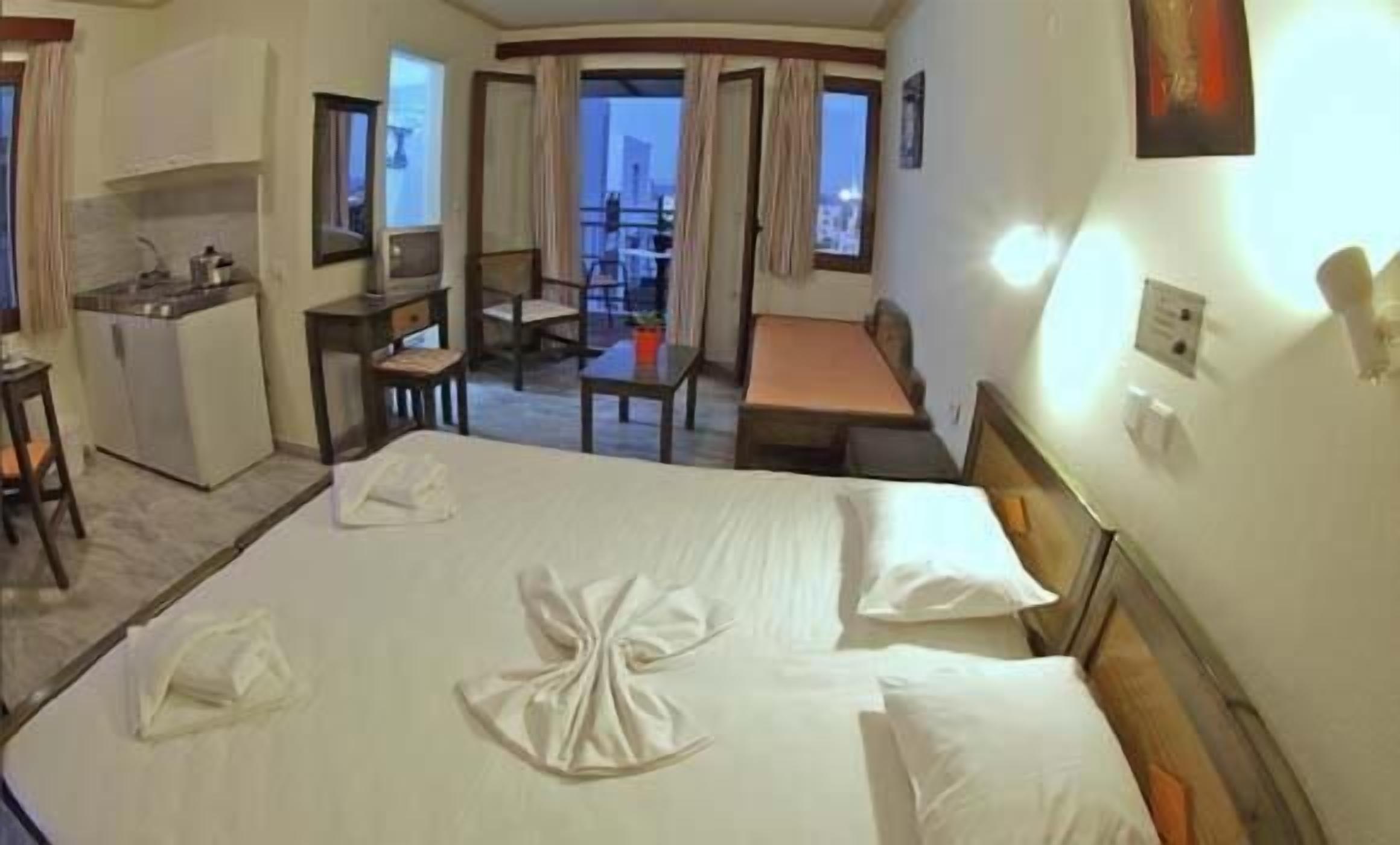 A hotel room with a bed, a desk, a chair, a small table, and a balcony with a view.
