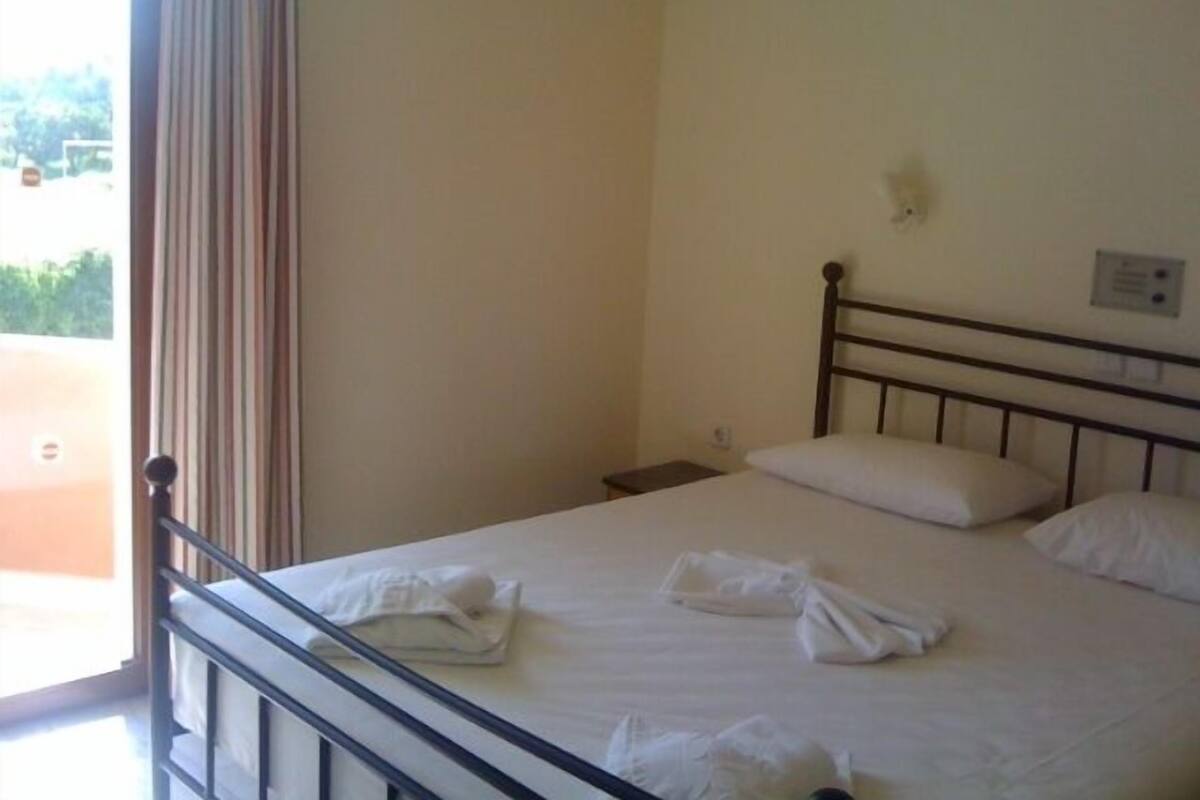 A single bed with white linens and pillows, a bedside table, and a window with curtains.