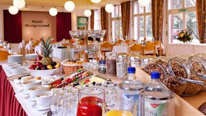 A breakfast buffet with various food items and beverages, a sign reading "Hotel Morgenland", and a view of the outside through large windows. - Hotel Morgenland (Berlin)