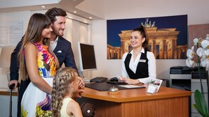 A reception desk with a receptionist, a computer, and a framed picture of a building. - Hotel Morgenland (Berlin)
