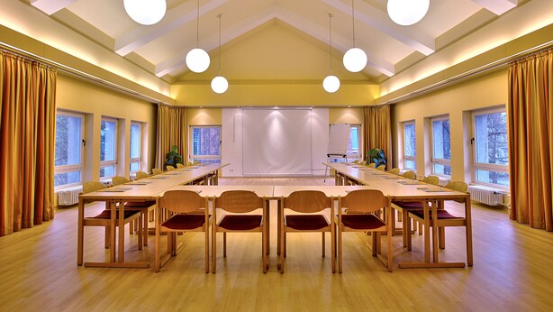 Una sala de conferencias con una larga mesa, sillas y una pantalla de proyección.
