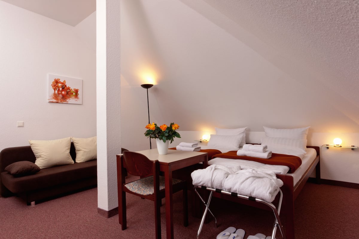 Quarto de hotel com cama, escrivaninha, cadeira, mesa pequena, sofá e obra de arte pendurada na parede.
