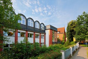 En moderne bygning med buede vinduer og en murstensfacade, omgivet af grønt og en sti.