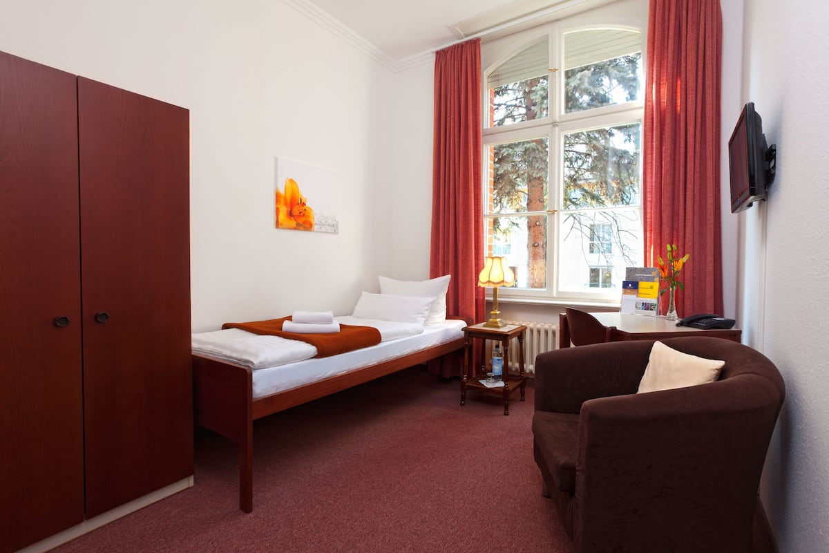 Quarto de hotel com cama, sofá, guarda-roupa de madeira, mesa com abajur e janela com cortinas.