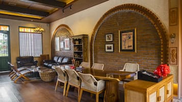 A spacious living room with a wooden dining table, comfortable seating, a brick fireplace, and a bookshelf.