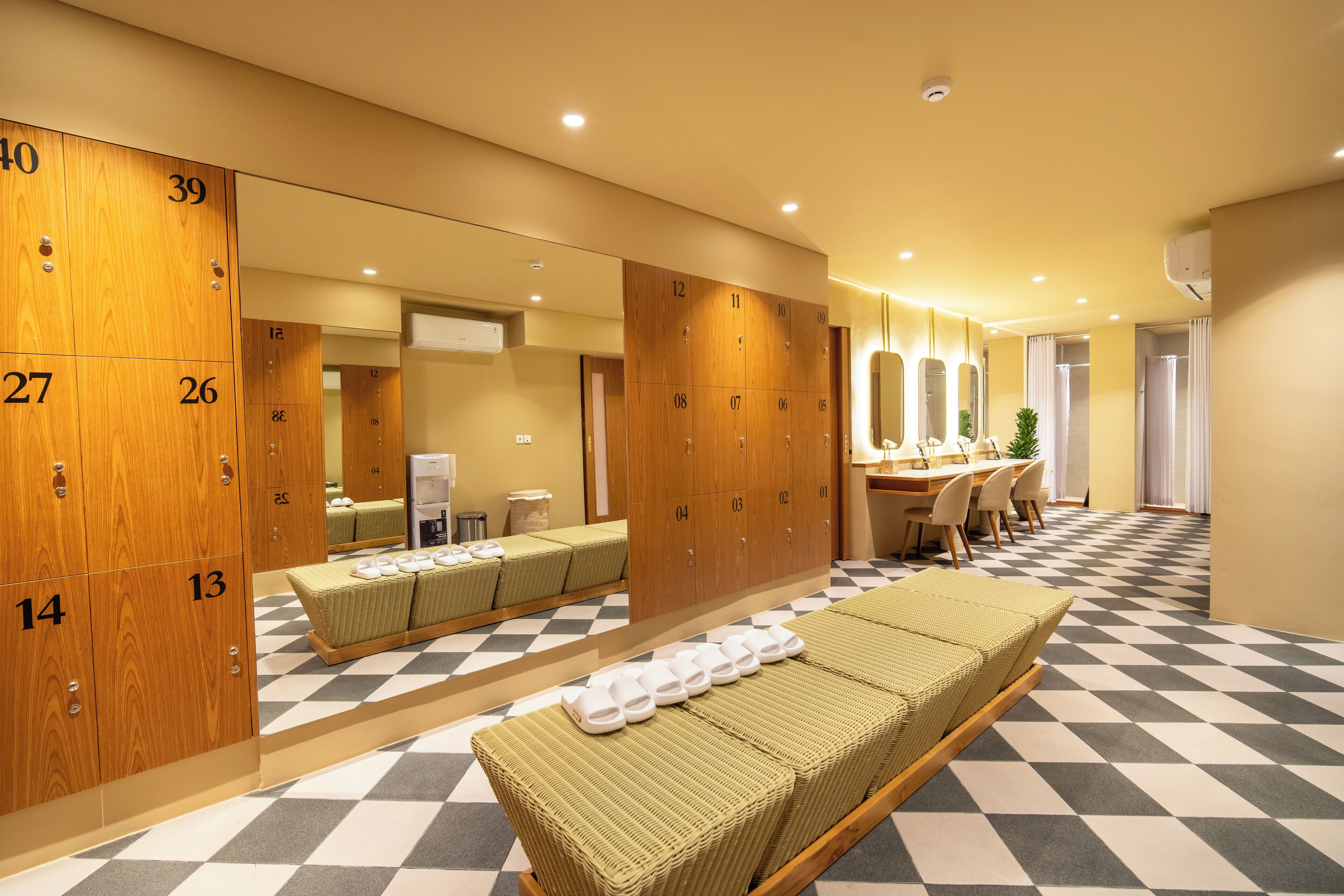 A hotel room with wooden lockers, a checkered floor, a bed, a desk, and a mirror.