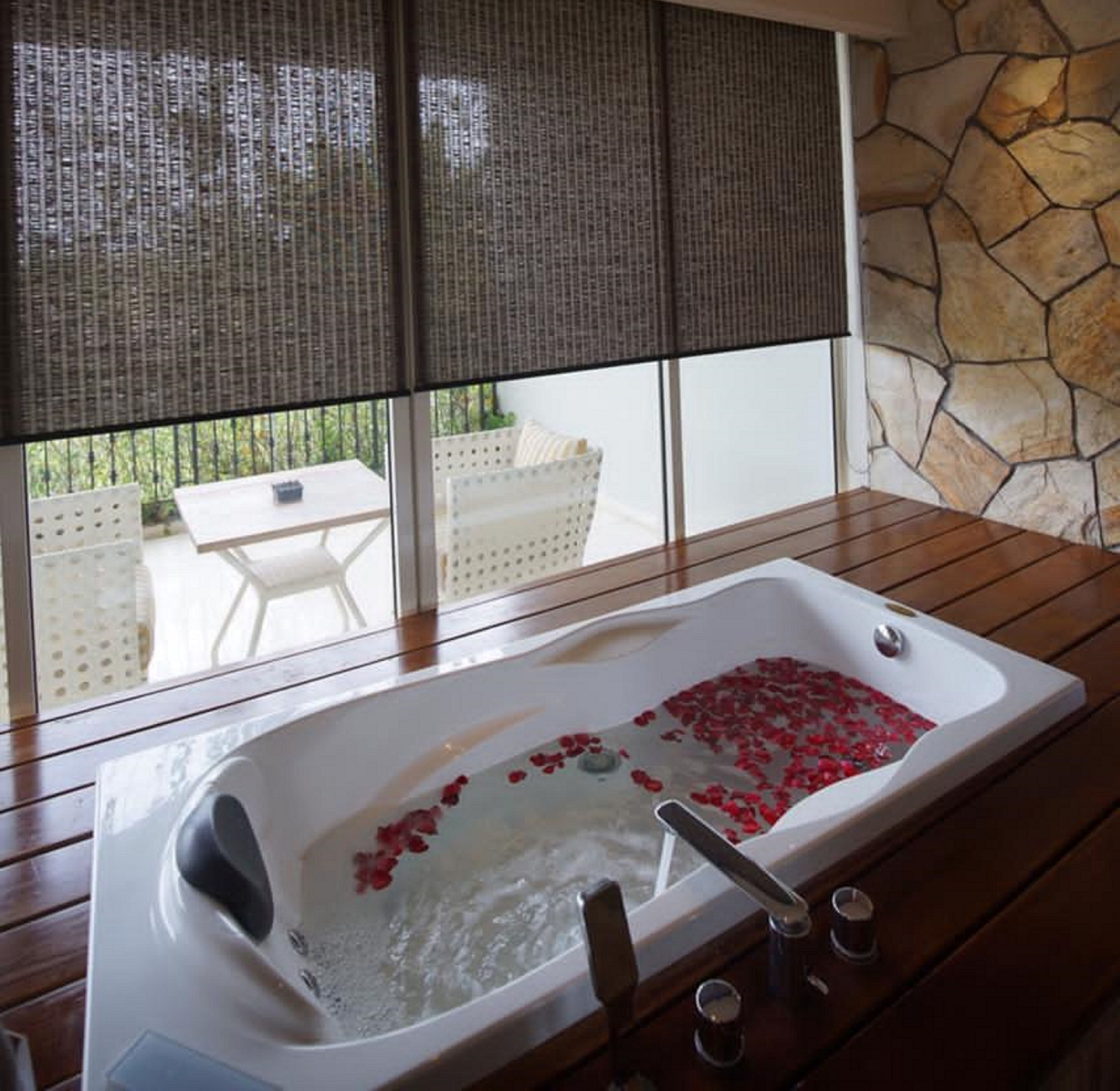 Una bañera con pétalos de rosa, una pared de piedra y vistas a muebles de exterior.