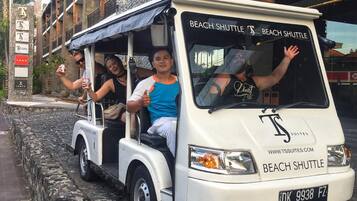 Ein Strandshuttlebus mit Fahrgästen, abgestellt auf einem Kopfsteinpflasterweg.