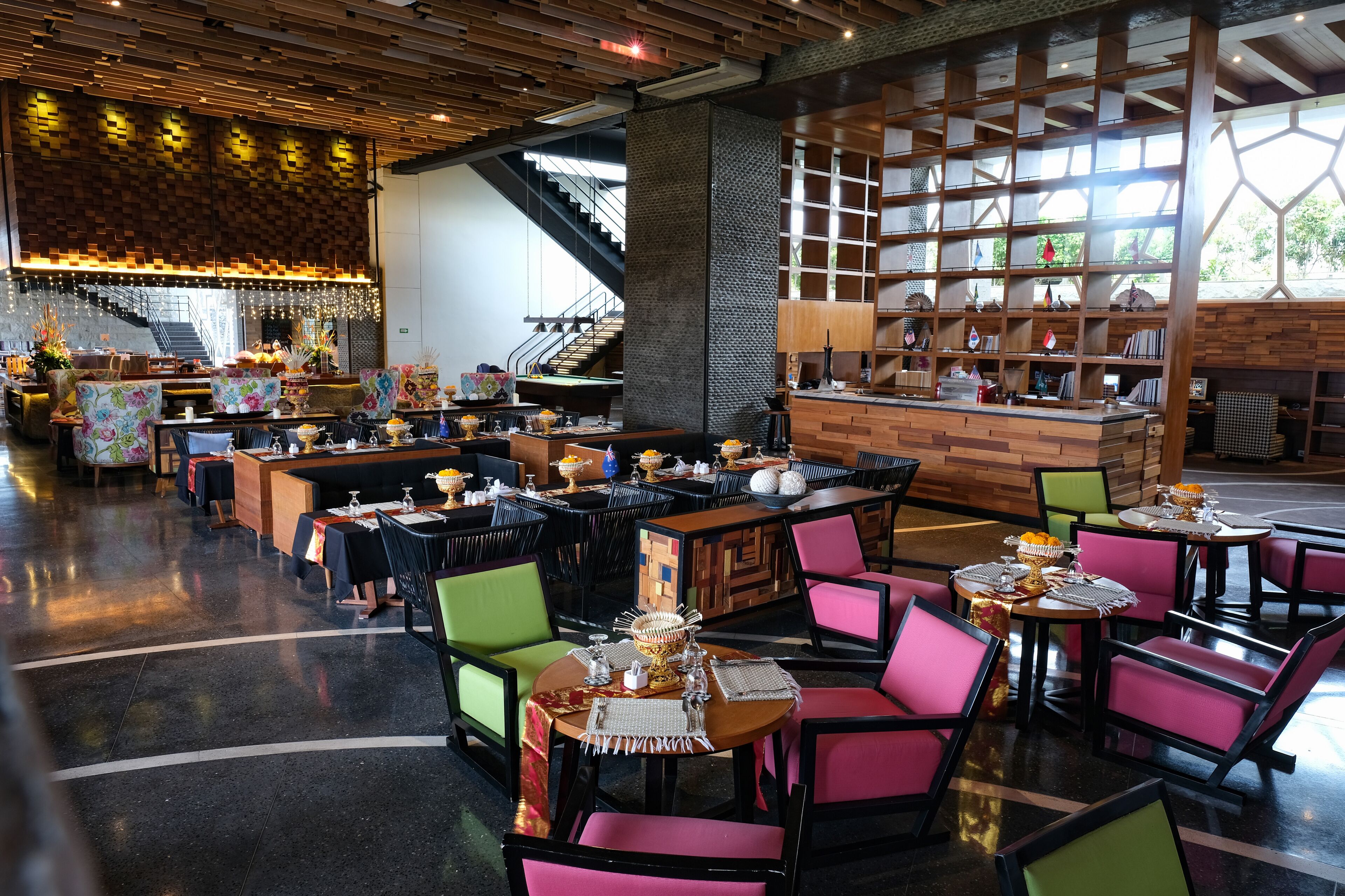 Ein Restaurant mit mehreren Tischen, Stühlen, einer Treppe und einem Bücherregal mit verschiedenen Gegenständen.