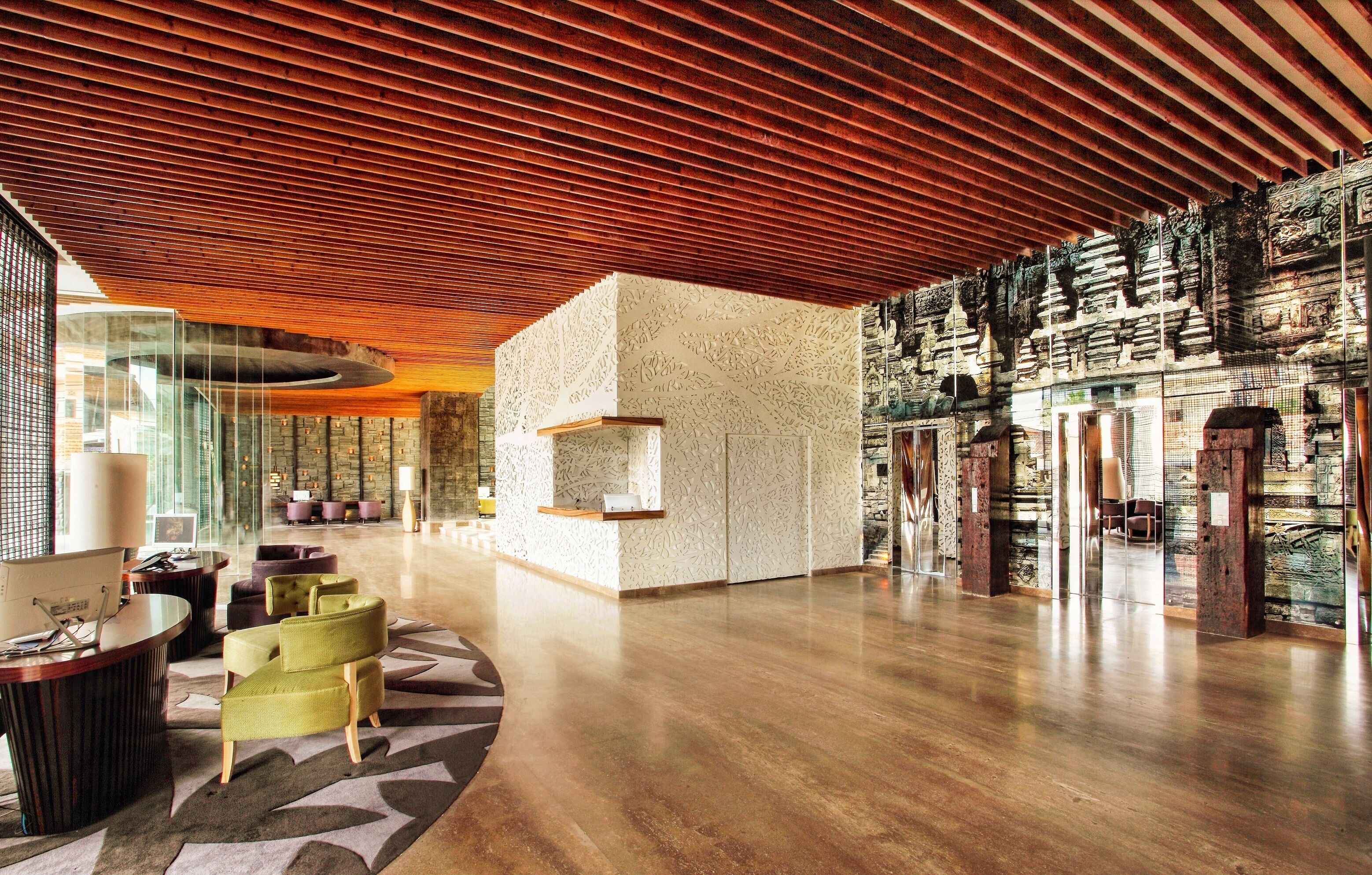 A spacious lobby with a wooden ceiling, a reception desk, seating area, and a wall with intricate carvings.