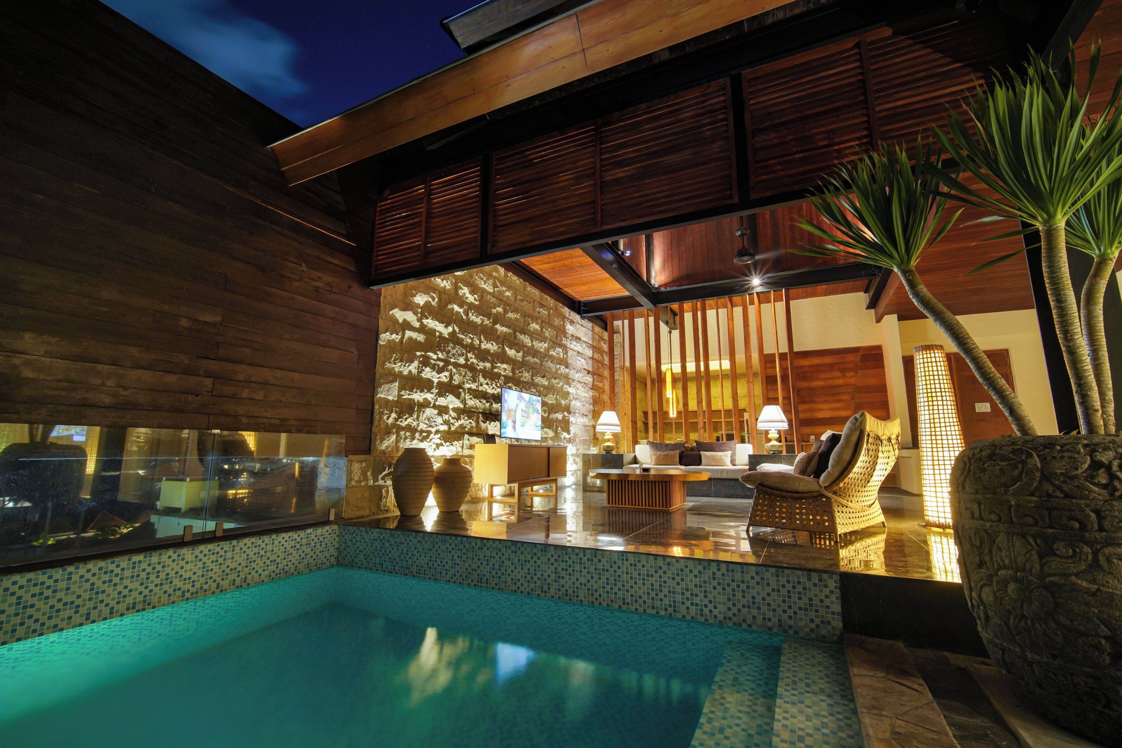 Uma área de piscina moderna com parede de pedra, assentos e uma televisão.
