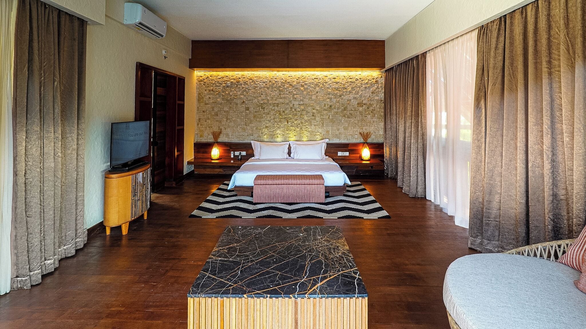 Una camera d'albergo con un letto grande, una TV, un comodino in legno e un tavolino da caffè in marmo.