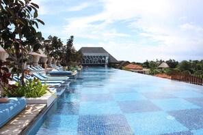 A long swimming pool with lounge chairs and potted plants along the sides. - TS Suites Seminyak (Legian)