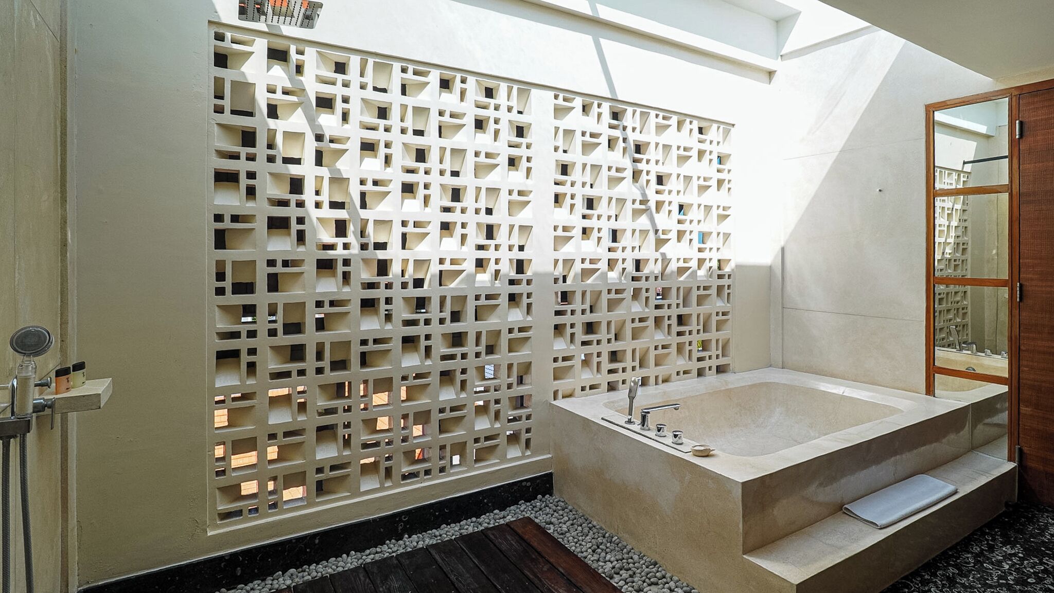 A modern bathroom with a freestanding bathtub, a wooden door, and a decorative wall with geometric cutouts.