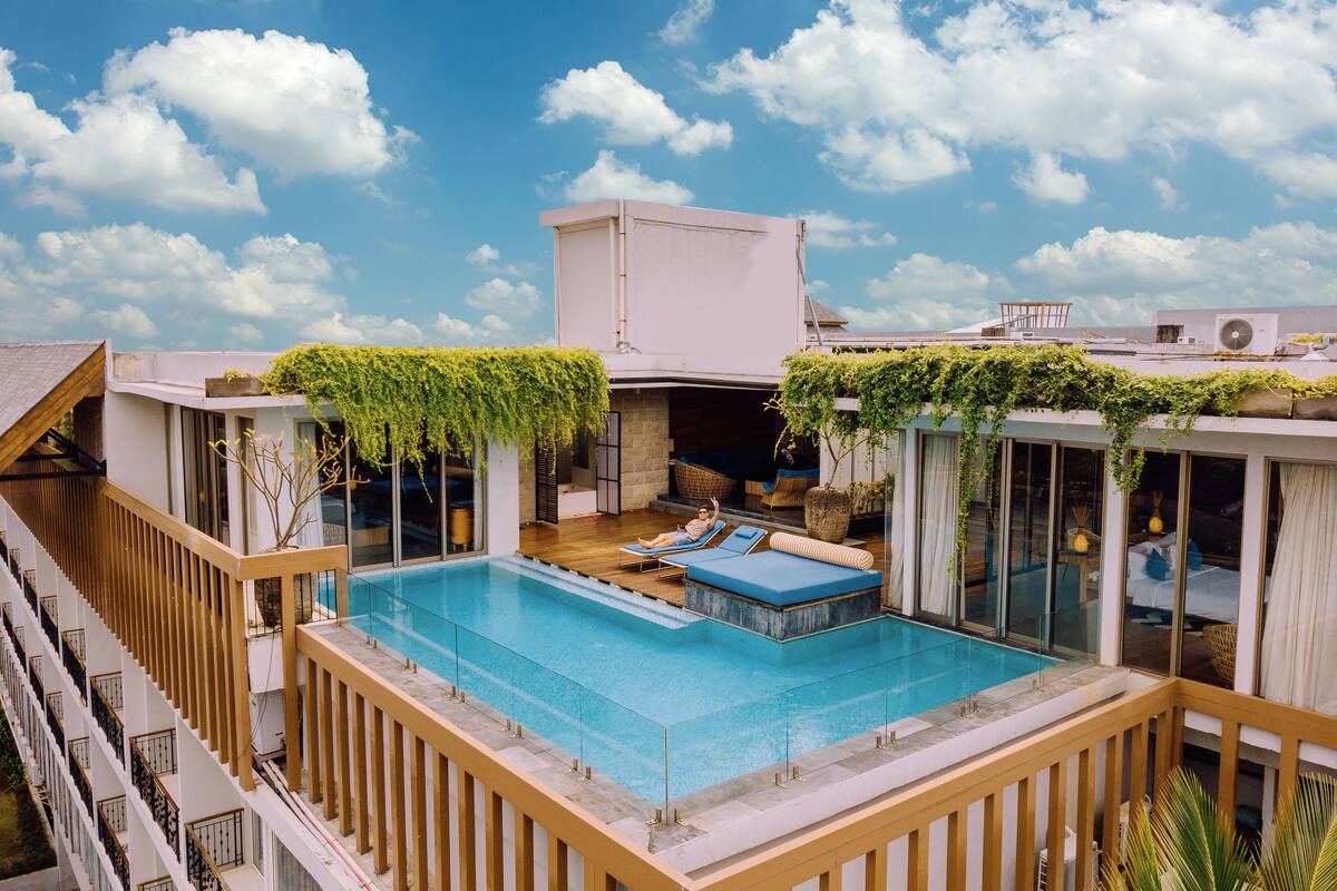 A rooftop pool with lounge chairs, a stone fireplace, and a view of the sky.