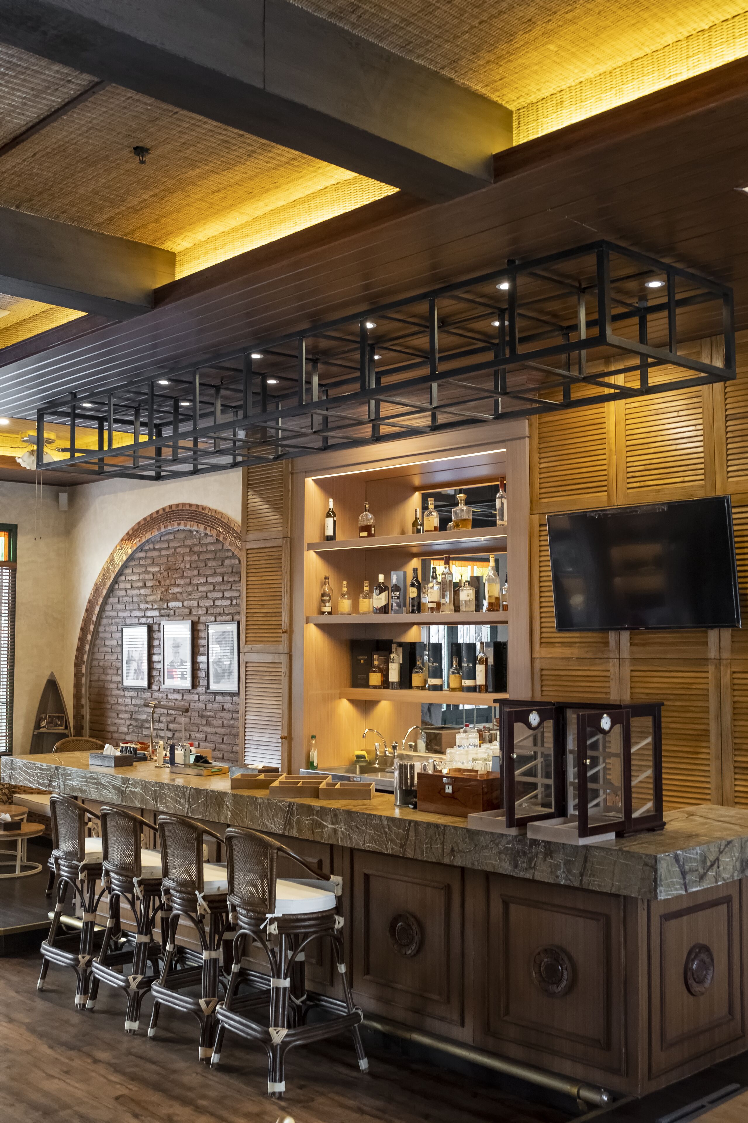 A bar area with a wooden counter, bar stools, shelves with bottles, and a flat-screen TV.