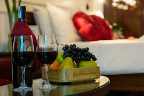 A table with a bottle of wine, two wine glasses, and a fruit basket.