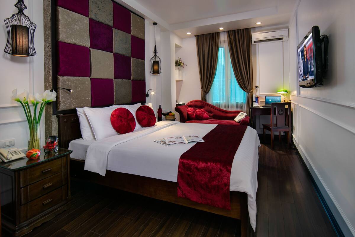 A modern hotel room with a large bed, a desk with a computer, and a television on the wall.