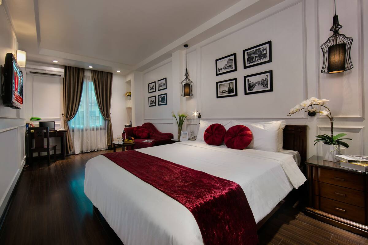 A hotel room with a large bed, a desk, a chair, and a small table with a vase of flowers.